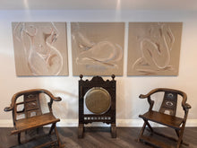 Load image into Gallery viewer, Three abstract figurative linen canvas paintings in beige and neutral tones hang on a white wall above a dark wooden gong and two matching wooden armchairs.